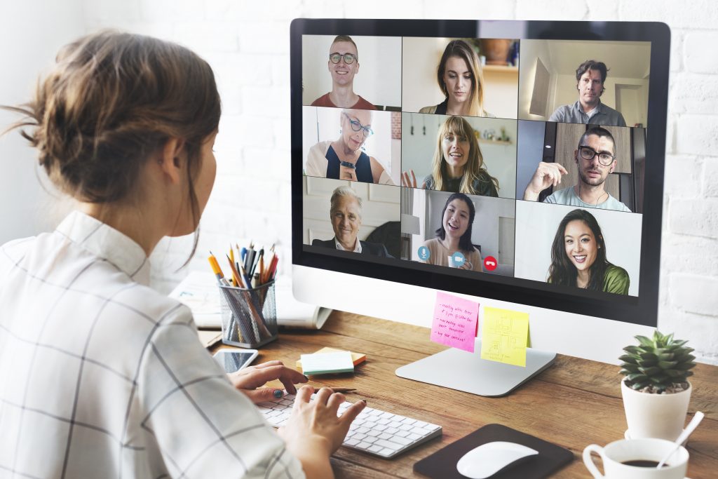 Person participating in a video conference with multiple attendees, practicing virtual meeting best practices at a well-equipped desk with office supplies