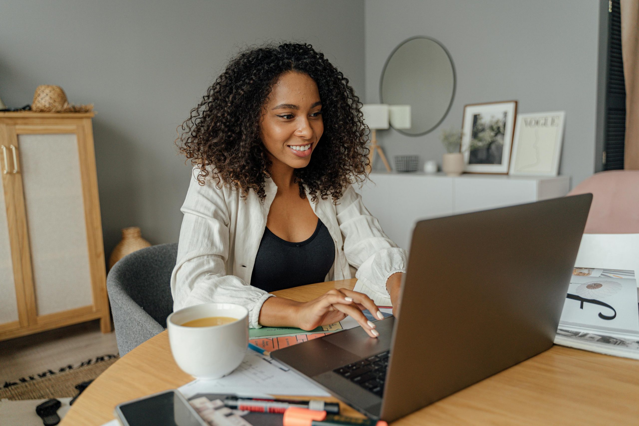 Professional woman smiling while typing on laptop, demonstrating audience-centered communication principles in a warm, modern home office setting
