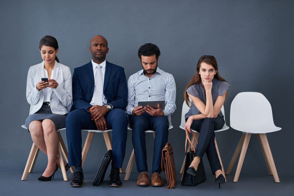 Four professionals sitting in a row, one visibly more stressed than the others, with an empty chair at the end of the row.